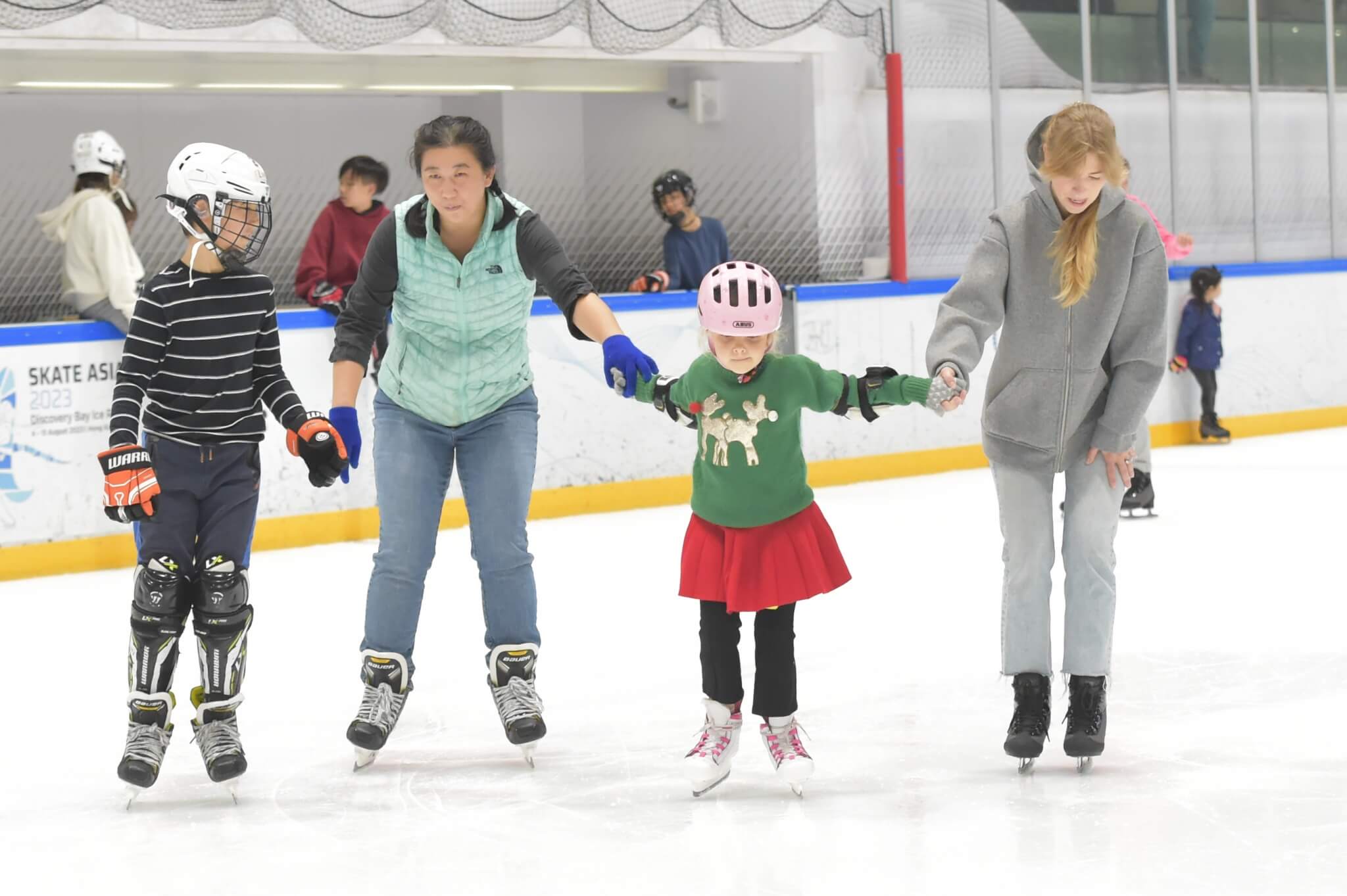 Mature women and kids ice skating while holding hands